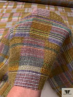 a person's hand is covered with multicolored fabric on a bed sheet