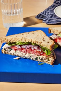 a cut in half sandwich sitting on top of a blue cutting board next to a glass of water