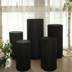 three black vases sitting next to each other in front of a window with white flowers