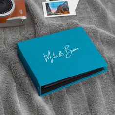 a blue book sitting on top of a bed next to a camera and polaroid