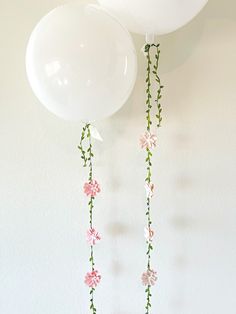 two white balloons hanging from the ceiling with pink flowers on them and green stems attached to each balloon