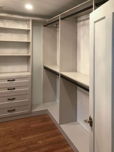 an empty walk in closet with white shelves and drawers on one side, wood flooring on the other