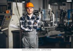 a man in an orange hard hat is standing with his arms crossed and looking at the camera