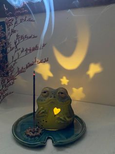 a lit candle sits on top of a frog shaped plate in front of a wall