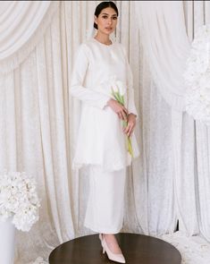 a woman standing in front of a white curtain holding a bouquet of flowers and posing for the camera