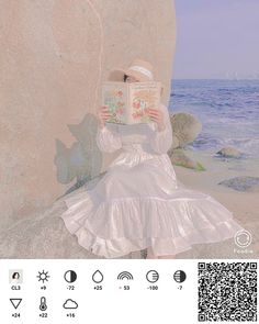 a woman sitting on top of a rock next to the ocean holding a book in her hands