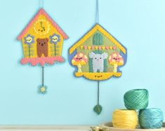 there are two little houses hanging on the wall next to balls of thread and yarn