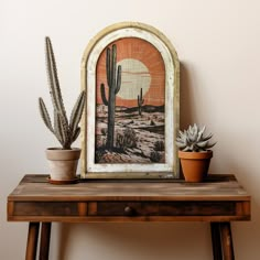 a cactus sits on a table next to an old picture frame and potted cacti