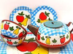 an old fashioned tea set on a checkered tablecloth with apples and lemons painted on it