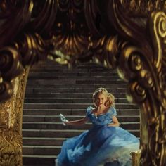 a woman in a blue dress sitting on top of a golden chair next to stairs