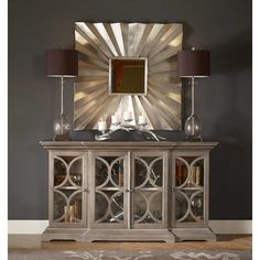 a cabinet with candles on it in front of a wall mounted mirror and two lamps