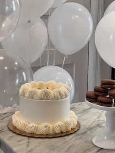 a white cake sitting on top of a marble counter next to balloons and plates filled with cookies