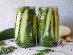 two mason jars filled with cucumbers and herbs