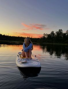 a woman sitting on top of a surfboard in the water at sunset or dawn