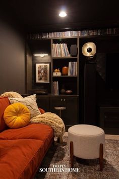 a living room with orange couches and bookshelves in the background, along with a white footstool