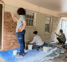 two people are painting a brick wall with paint rollers and buckets on the floor