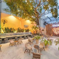 an outdoor restaurant with tables and chairs under a tree in the center, surrounded by greenery