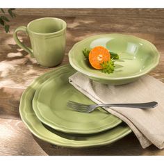 a green plate topped with an orange next to a cup and saucer on top of a wooden table