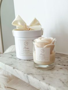 two candles sitting on top of a marble counter next to a white container with a bow