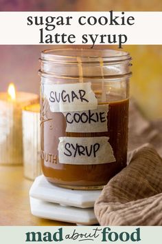 a jar of sugar cookie syrup sitting on top of a table next to a candle