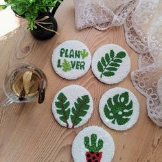 four embroidered coasters on a table next to a glass of wine and potted plant