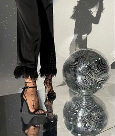 a woman standing next to a shiny disco ball on top of a black table in front of a mirror