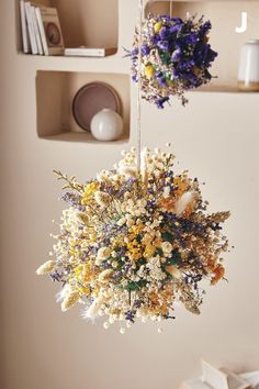 two hanging baskets filled with dried flowers on top of a wooden table next to bookshelves