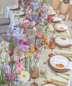 a long table is set with flowers and gold place settings for dinner guests to enjoy