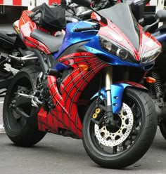 a red, blue and black motorcycle parked on the side of the road next to other motorcycles