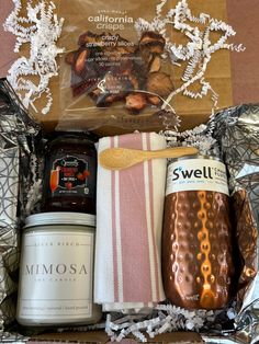 an assortment of food and drink items in a gift box with foil wrapping around it