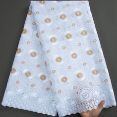 a hand is holding up a piece of white and gold fabric with circles on it