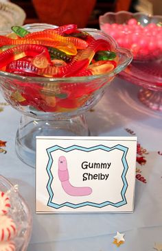 there is a bowl full of gummy worms on the table next to some candy