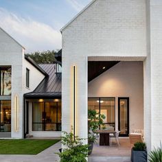 a modern house with white brick walls and black trim on the windows, grass in front of it