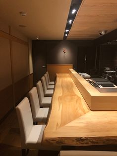 a long wooden counter with white chairs in front of it