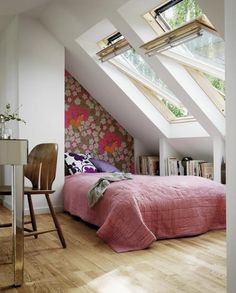 an attic bedroom with pink bedspread and floral wallpaper on the walls, along with wooden flooring