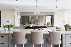 a kitchen island with four chairs and an oven in the back ground, surrounded by potted plants