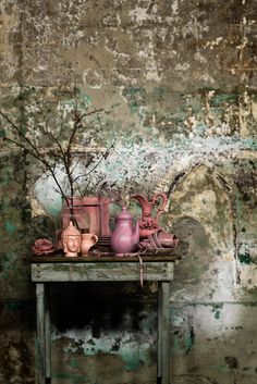 an old table with vases and other items on it in front of a dirty wall