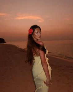 a beautiful woman standing on top of a sandy beach next to the ocean at sunset