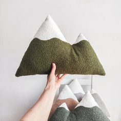 a person is holding up a pillow made out of green and white pillows with mountains on them