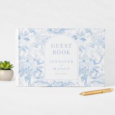 a guest book next to a pen and succulent plant on a white surface