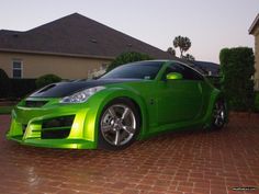 a green sports car is parked in front of a house on a brick driveway area