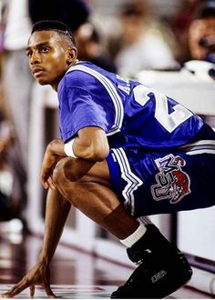 a basketball player crouching down on the court with his hands in his pockets and knees bent