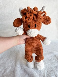 a hand holding a small brown and white stuffed animal