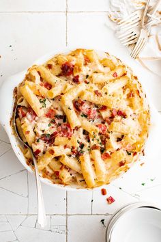 a bowl filled with pasta and sauce on top of a white tiled floor next to silverware