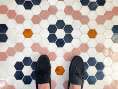 a person's feet in black shoes standing next to a tiled floor with hexagonal tiles