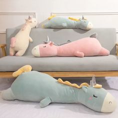 three stuffed animals sitting on top of a gray couch next to pillows with unicorns