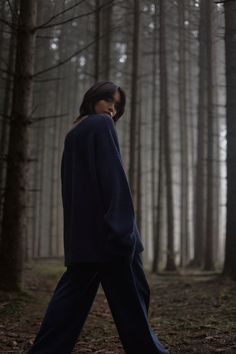 a woman walking through the woods in front of trees