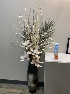 a black vase filled with white flowers on top of a wooden table next to a wall