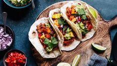 three tacos on a cutting board with salsa and avocado