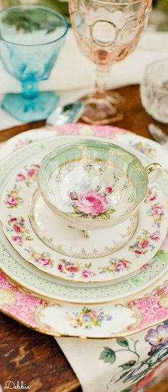 a table topped with plates and bowls filled with flowers on top of each other next to glasses